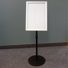 A white sign on a stand in front of a wall.
